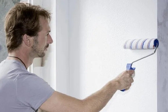 Person streicht Wand mit Farbrolle